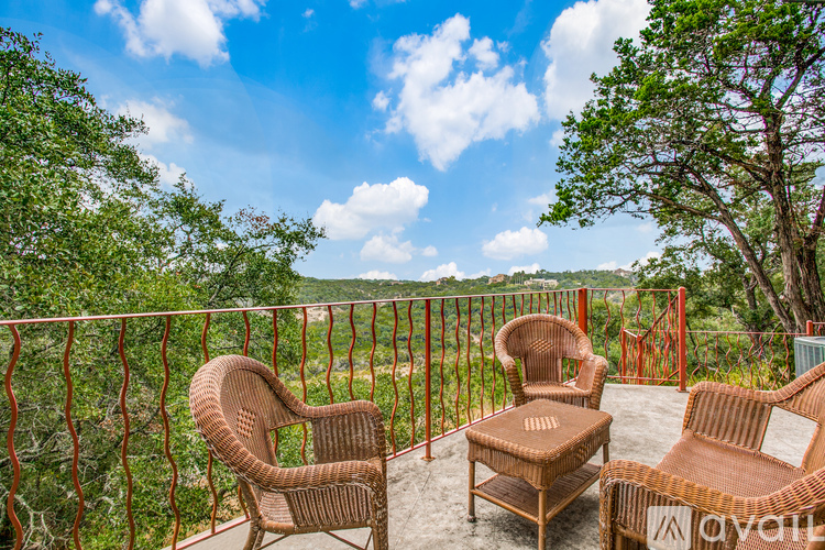Three wicker chairs are placed on a balcony with a view of the trees and sky.
