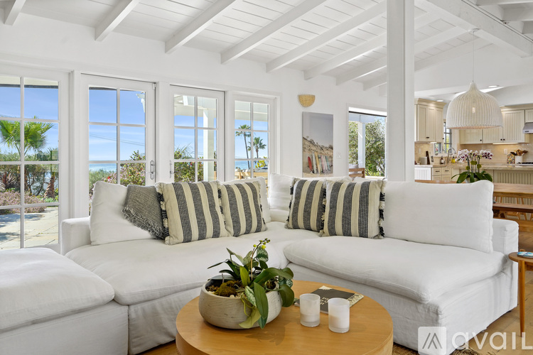 A living room with white furniture and a view of the beach.