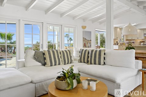A living room with white furniture and a view of the beach.