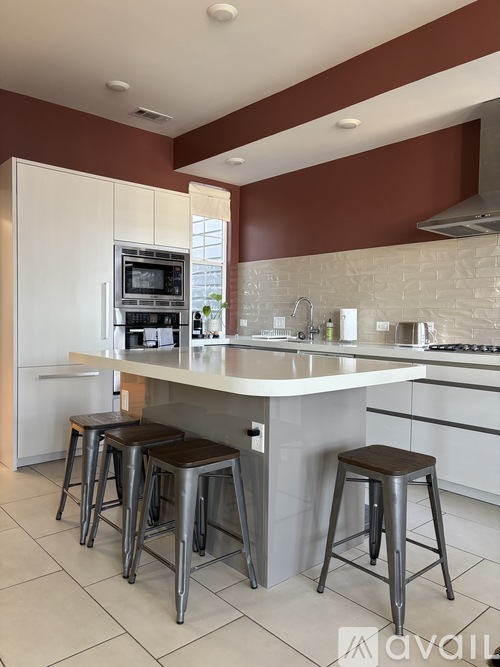A kitchen with white cabinets and a white island with brown stools.