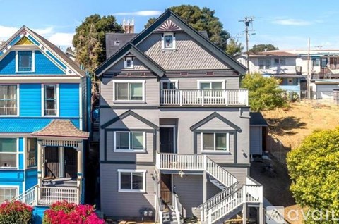 A blue house with a porch is in front of a grey house.