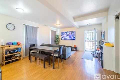 A living room with a dining table and chairs, a clock on the wall, and a flat-screen TV mounted above the TV stand.