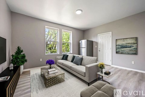 A living room with a grey couch, a glass coffee table, and a painting on the wall.