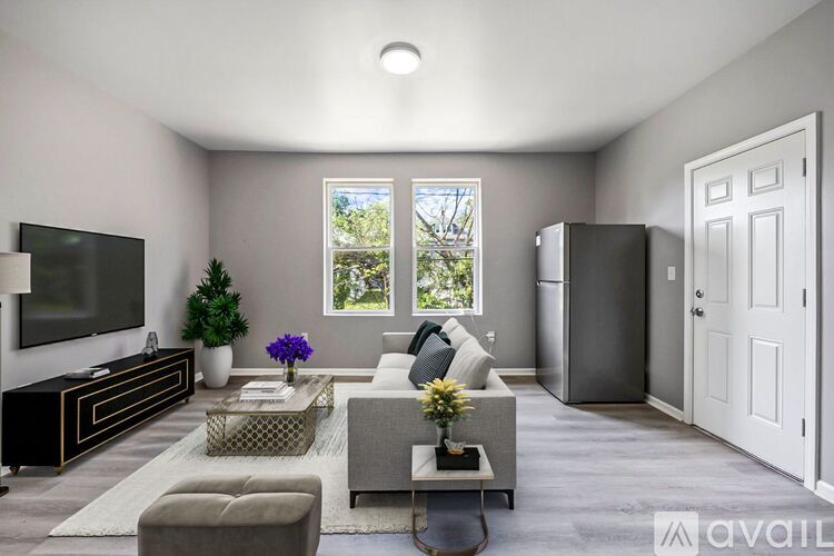 A living room with a grey couch, a glass coffee table, a television, and a plant.