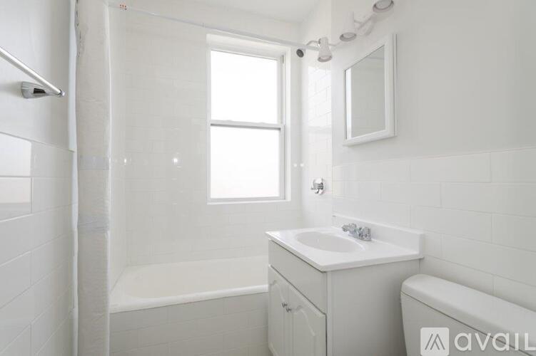 A white bathroom with a tub, sink, mirror, and window.