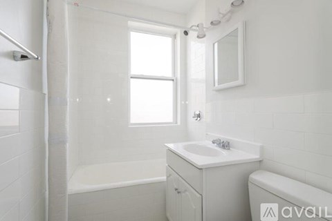 A white bathroom with a tub, sink, mirror, and window.