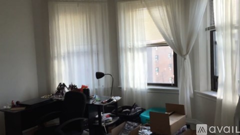 A room with a desk, chair, and a window with curtains.