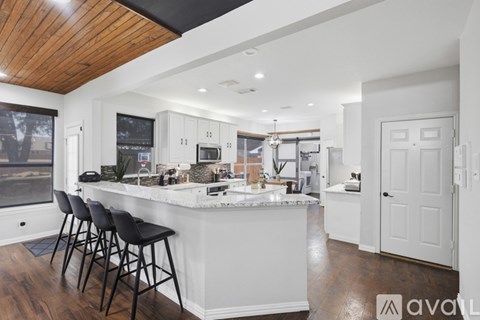 A kitchen with white cabinets and a bar area with black stools.