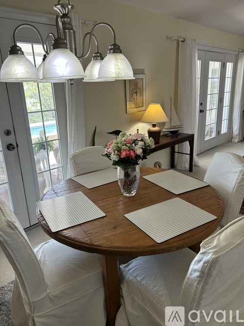 A dining room with a round wooden table surrounded by white chairs.