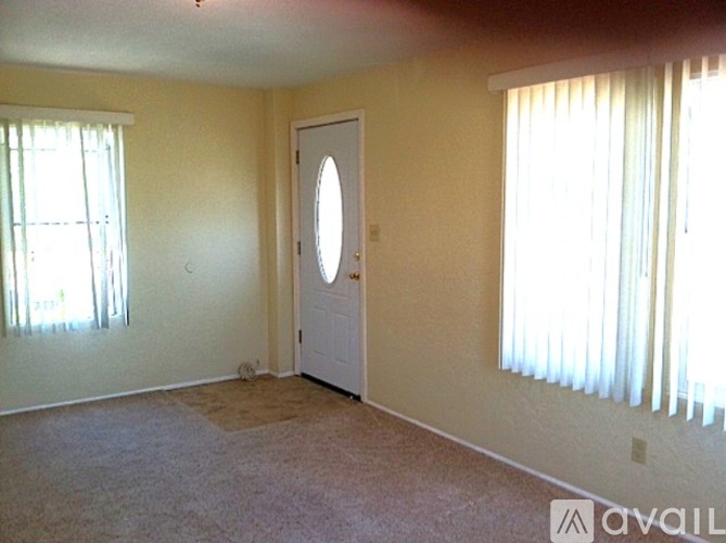 A room with a white door and two windows with white curtains.