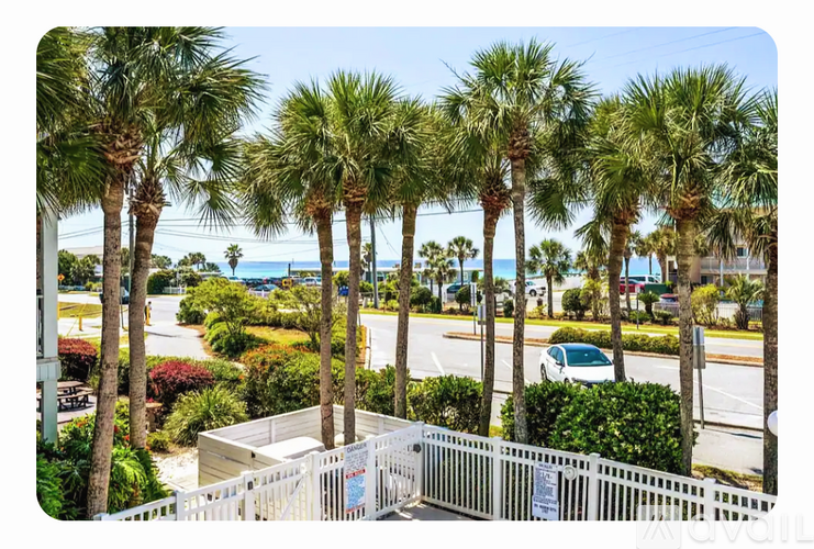 A white fence with a sign on it in front of some palm trees.