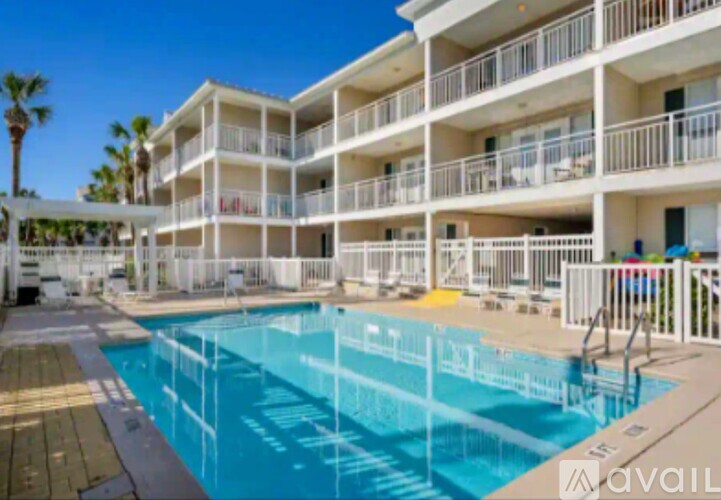A large swimming pool is surrounded by a white fence and a building with balconies.