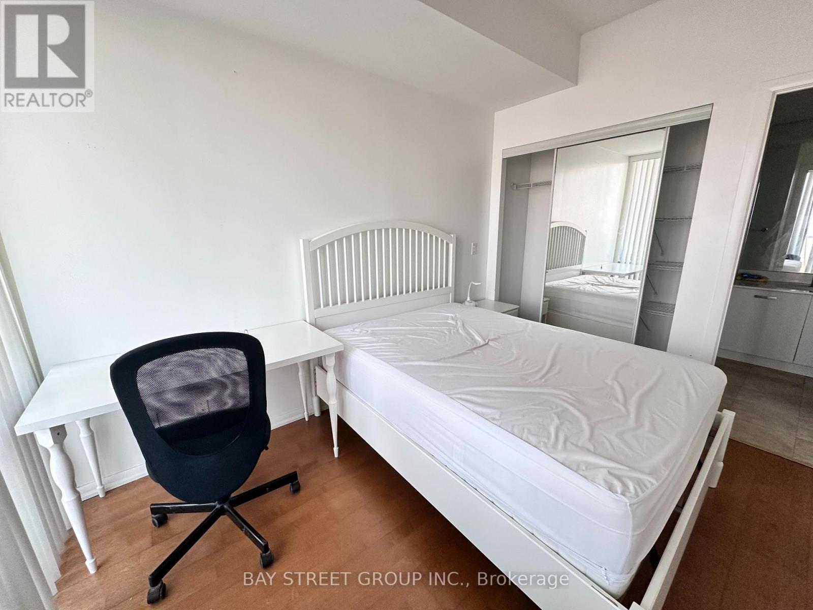 A bedroom with a white bed, a chair, and a mirror.