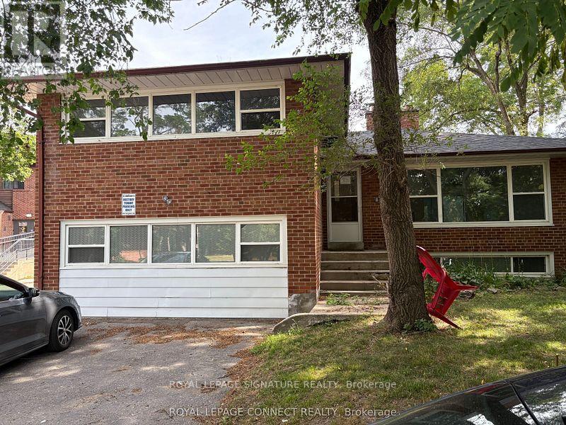A red chair is placed on the grass in front of a brick house.