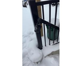 A black railing with a green container in the background.