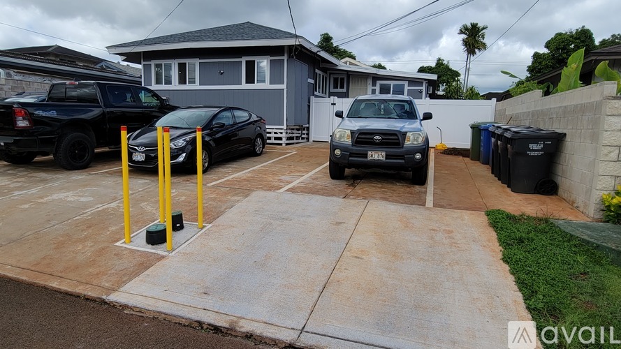 A black car is parked in a driveway next to a yellow pole.