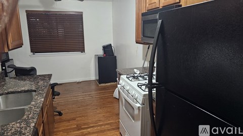 A black refrigerator is in the corner of a kitchen with a stove and microwave.