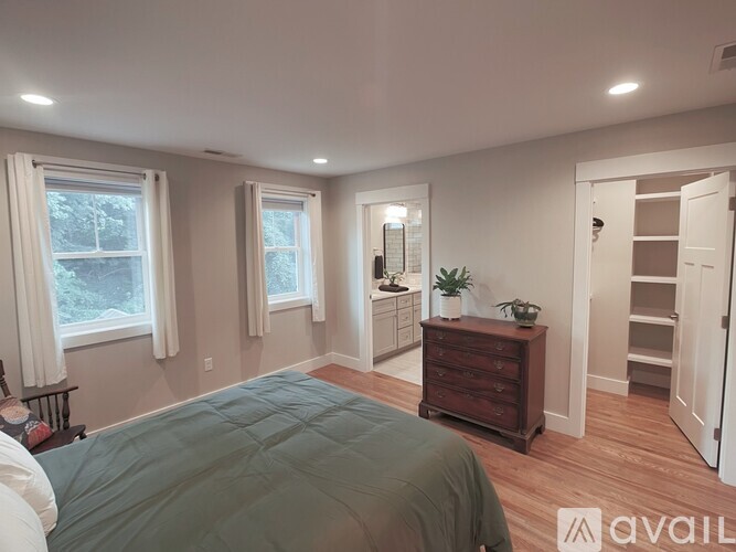 A bedroom with a bed in the foreground and a dresser with a mirror above it in the background.