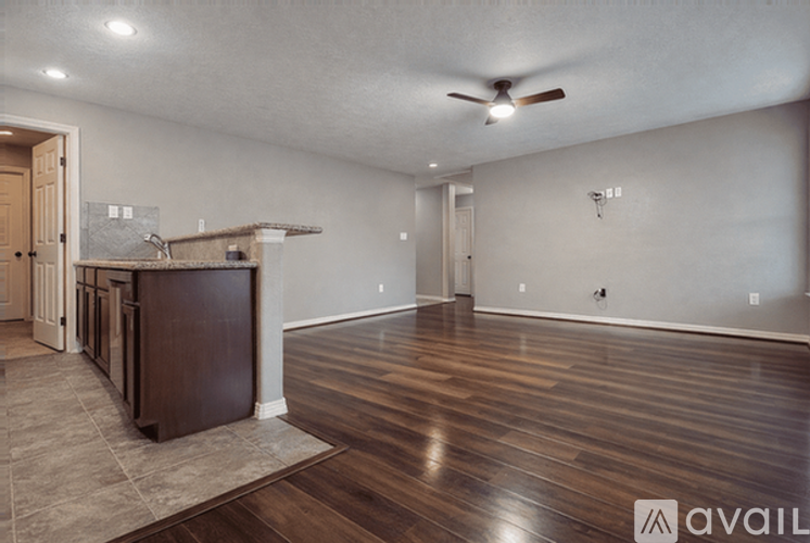 A spacious room with wooden floors and a kitchen area with a bar.
