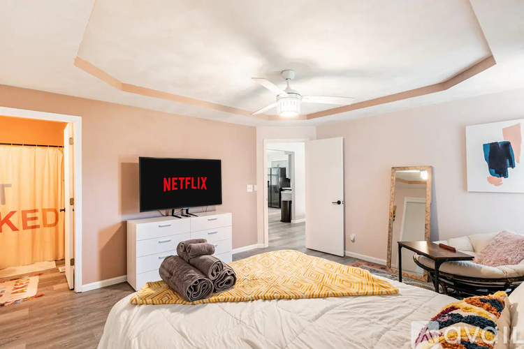 A bedroom with a bed, a TV displaying the Netflix logo, and a chair.