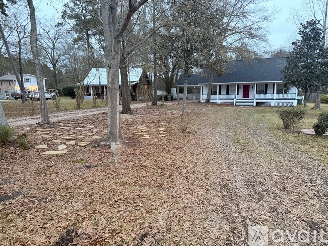 A white house with a red door is surrounded by trees and shrubs.