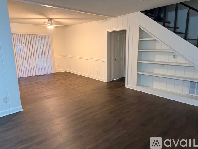 A spacious room with wooden flooring and a staircase on the right side.