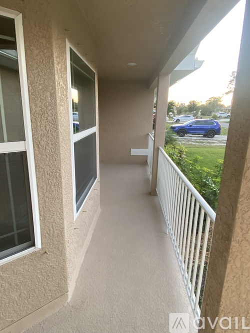 A balcony with a white railing and a view of a blue car and trees.