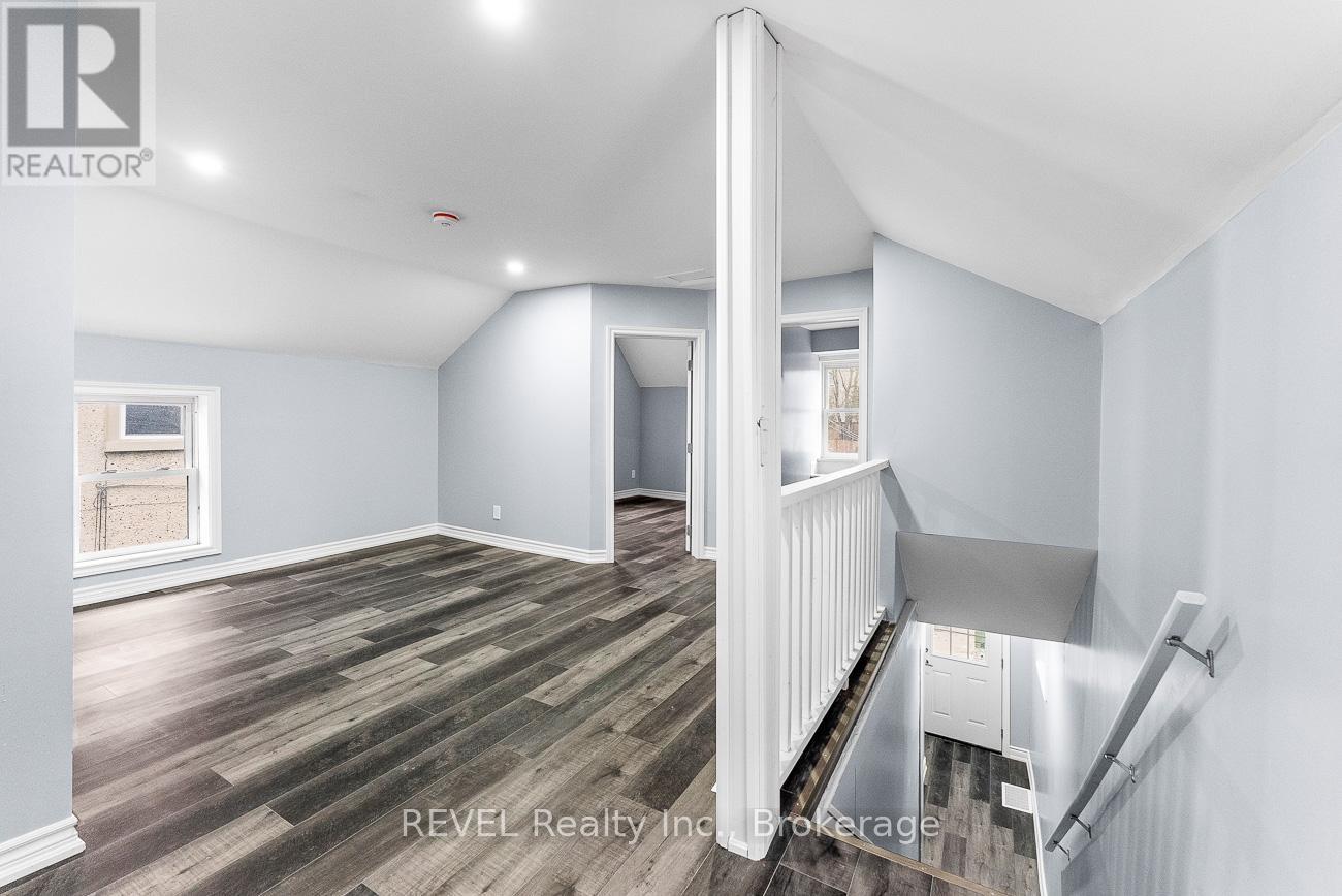 A room with wooden flooring and white walls, with a staircase on the right side.