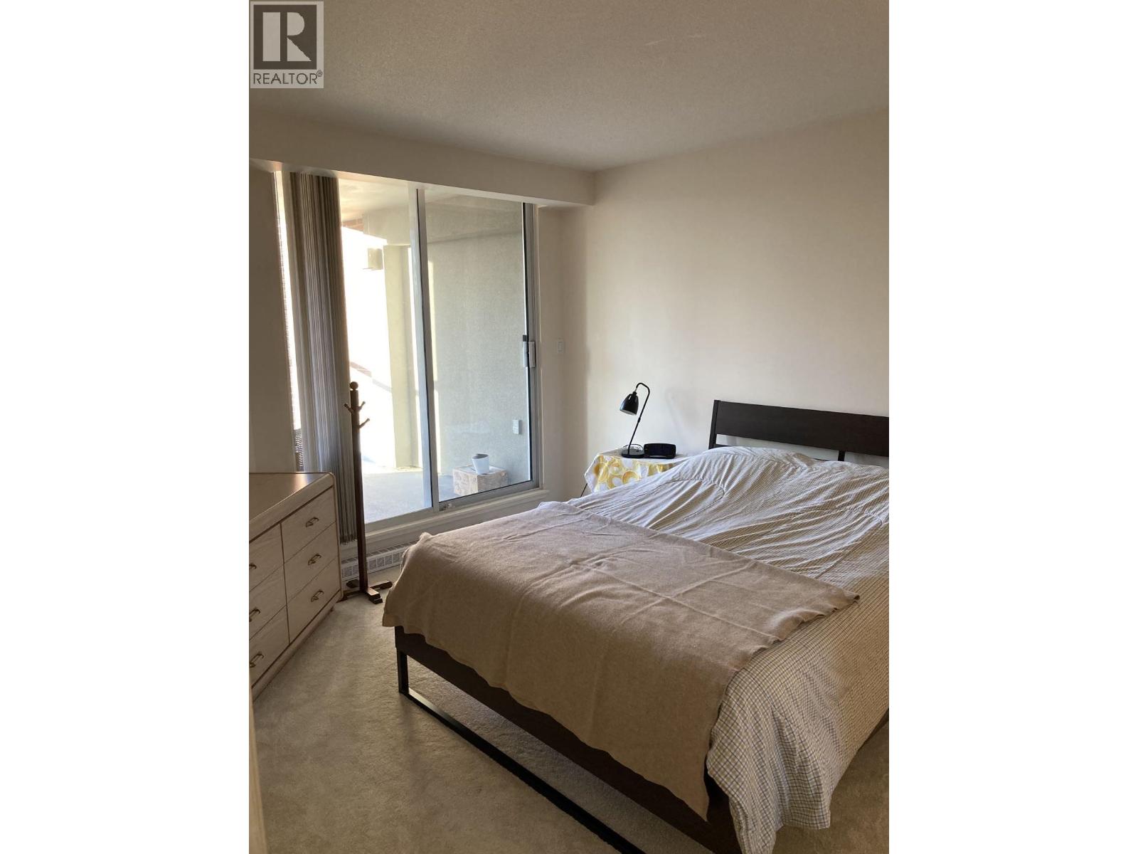 A bedroom with a bed, nightstand, and a window with curtains.