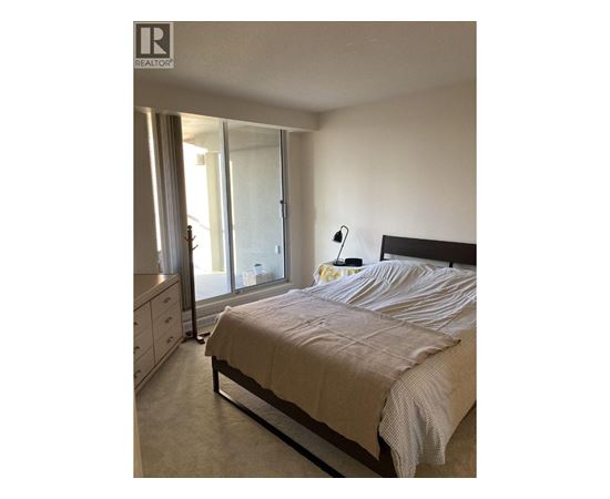 A bedroom with a bed, nightstand, and a window with curtains.