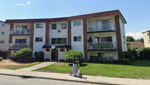 A person is riding a scooter in front of a building.