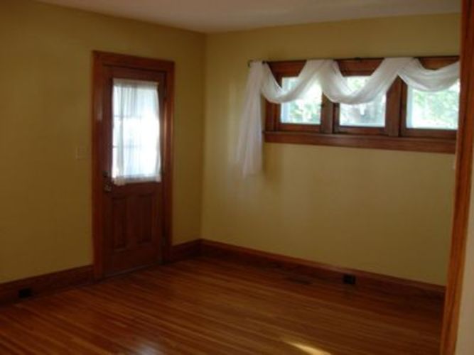 A room with a wooden floor and a window with white curtains.