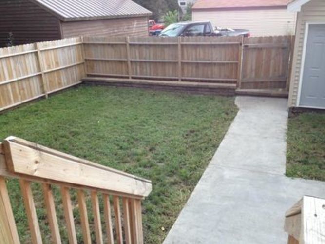 A backyard with a wooden fence and a concrete walkway.