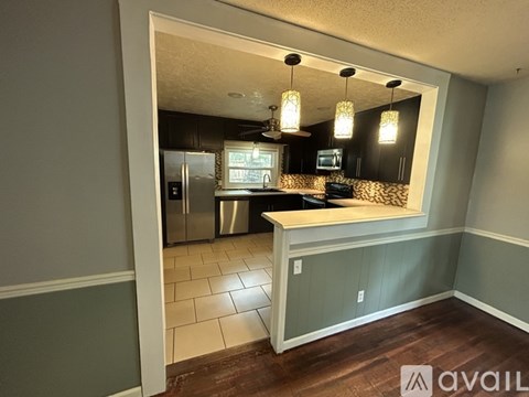 A kitchen with a refrigerator, stove, and cabinets is shown through an open doorway.
