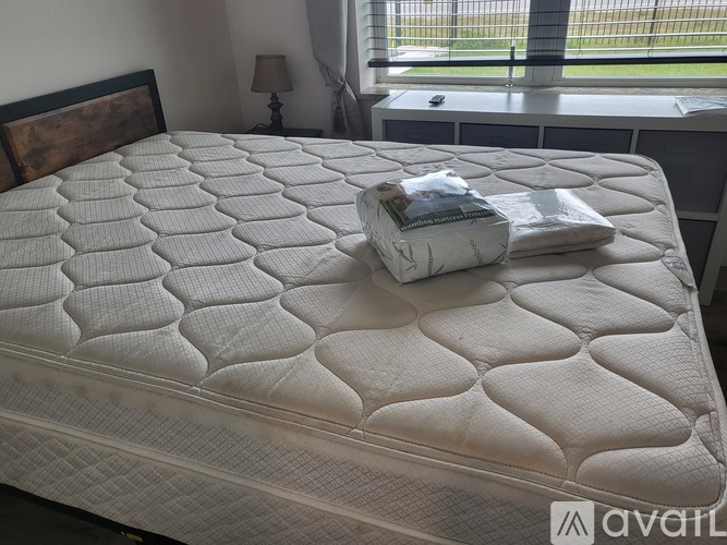 A bed with a white mattress and a brown pillow with a book and a tissue on it.