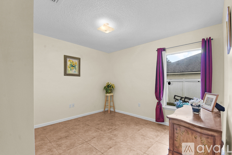 A room with a window, a plant on a stand, a picture frame, and a wooden dresser.
