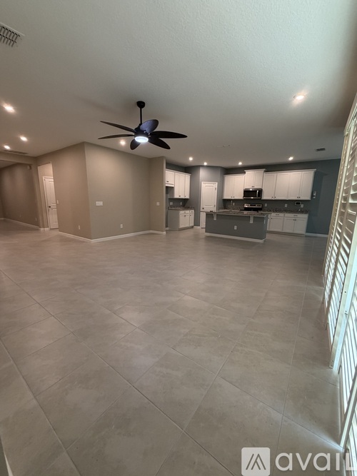 A spacious living room with a ceiling fan and a kitchen area in the background.