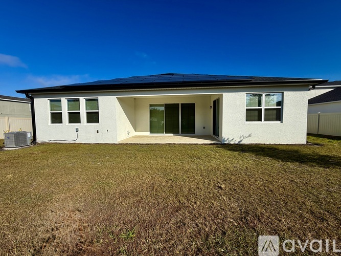 A house with a white exterior and a black roof is surrounded by a grassy area.