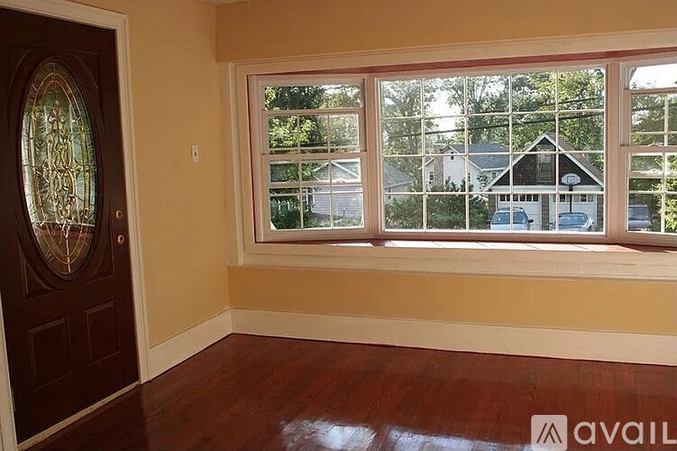 A room with a wooden floor and a window showing a house and cars outside.