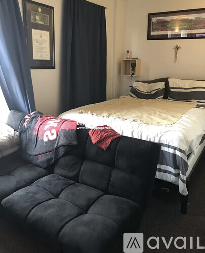 A bedroom with a bed, a black chair, and a framed picture on the wall.