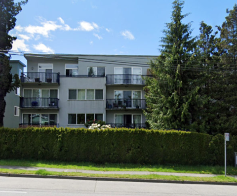 Apartment building with balconies and a hedge in front.