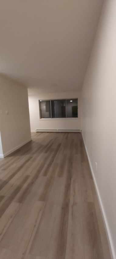 A long, empty hallway with wooden floors and white walls.