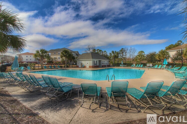 A pool surrounded by chairs and trees with a building in the background.