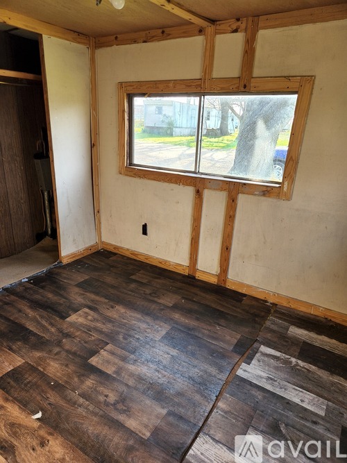 A room with wooden flooring and a window is under construction.