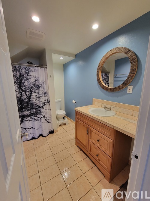 A bathroom with a blue wall and a round mirror above a sink.