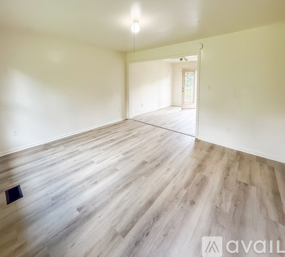 A spacious room with wooden flooring and a doorway leading to another room.