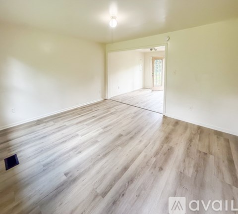 A spacious room with wooden flooring and a doorway leading to another room.