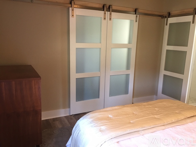 A bedroom with a bed, wooden dresser and frosted glass doors.