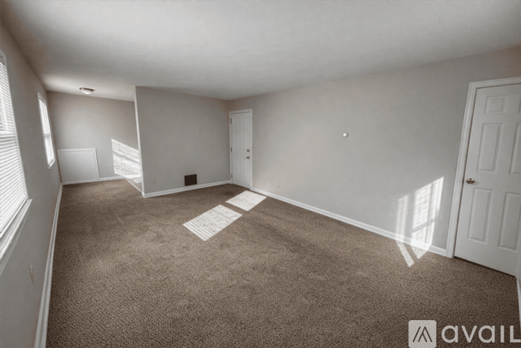 A room with carpeted floor and white walls, with a window on the left side.