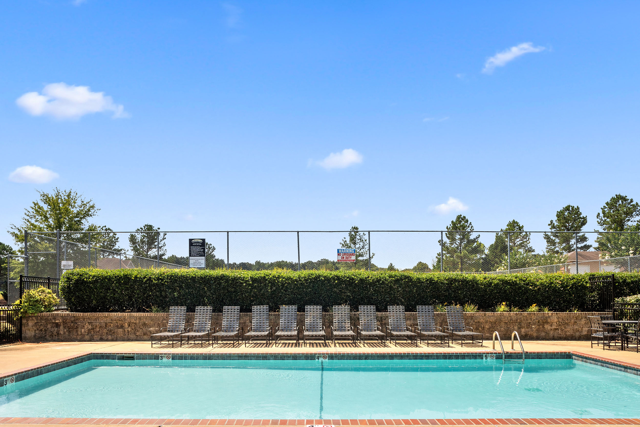 Lounge chairs next to privacy hedge, poolside at apartment swimming pool